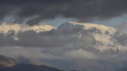 Snowy mountains of Sierra Nevada emerging between black clouds