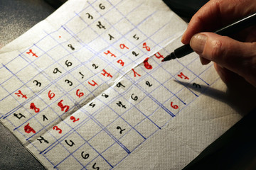 adult hand and marker pen making a sudoku with red and black numbers on a paper napkin