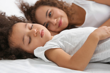 African-American mother with sleeping daughter lying on bed
