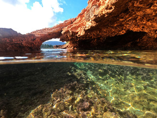 Underwater above and below photo of rocky seascape arch forming a beautiful emerald lagoon in tropical exotic island