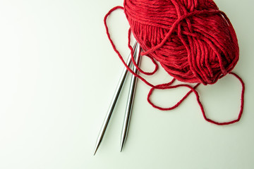 Knitting needles with red cotton yarn on a white background