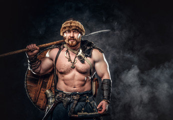 Fototapeta na wymiar Severe barbarian in warrior clothes, posing on a dark background.