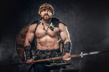 Severe barbarian in warrior clothes, posing on a dark background.