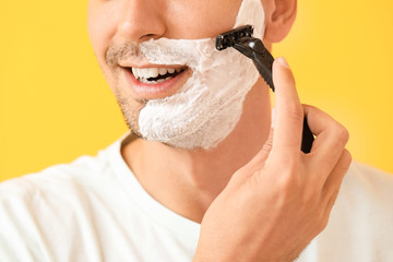 Handsome young man shaving against on color background, closeup