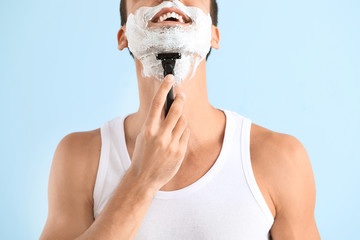 Handsome young man shaving against on color background