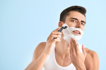 Handsome young man shaving against on color background