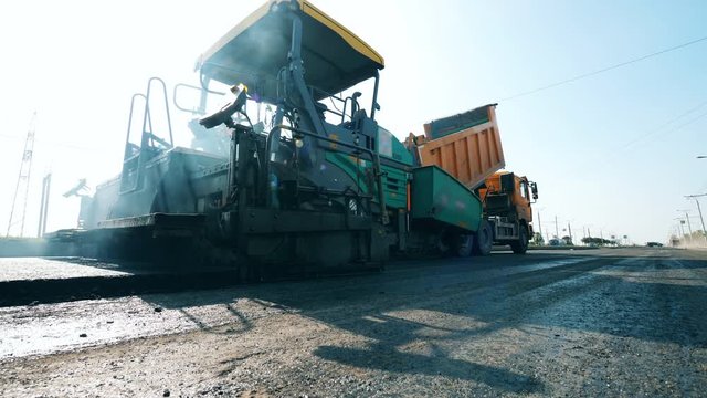 Road construction process. Bitum is being transported from the truck into the spreader