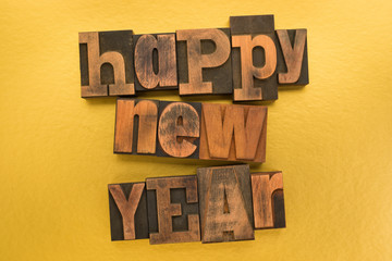 Happy new year written with vintage letterpress printing blocks on gold colored background
