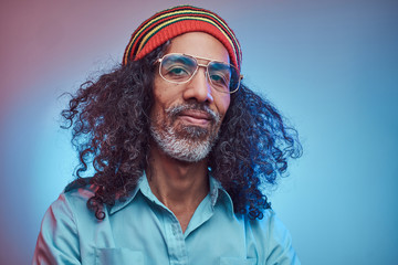 Smiling African Rastafarian male wearing a blue shirt and beanie. Studio portrait on a blue...