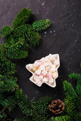 Marshmallows in Christmas tree shape plate on dark background with fir tree green branches. Smores for coffee or hot chocolate, copy space