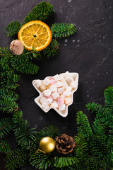 Obraz na płótnie Canvas Marshmallows in Christmas tree shape plate on dark background with fir tree green branches. Smores for coffee or hot chocolate, copy space
