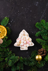 Marshmallows in Christmas tree shape plate on dark background with fir tree green branches. Smores for coffee or hot chocolate, copy space