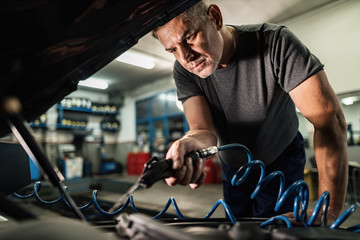 Mid adult auto mechanic cleaning car engine with air blow gun at repair shop.