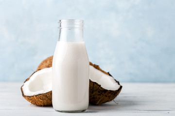 Health content, coconut milk in a glass bottle, coconut halves, light wooden table, close-up,