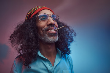 Happy African Rastafarian male smoking cigarettes. Isolated on a blue background.