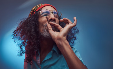 African Rastafarian smokes weed and gets high. Isolated on a blue background.