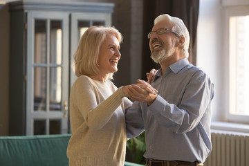 Cheerful elderly spouses dancing enjoy free time at home