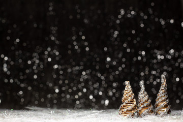 Christmas three wooden tree colored in solver glitter at the tips of the right site on dark background with silver and gold color bokeh and snoflakes at the battom. Holiday concept with copy space