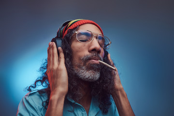 Studio portrait of African Rastafarian male enjoys music in headphones and smoking weed. Isolated...