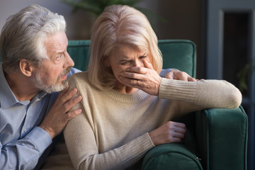 Elderly spouses indoors desperate wife crying worried husband comforting her