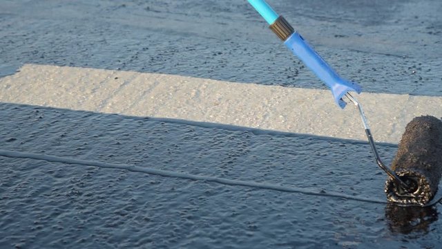 Waterproofing coating. Worker applies bitumen mastic on the foundation. Roofer cover the rooftop polymer modified bitumen waterproofing primer, with a roller brush.
