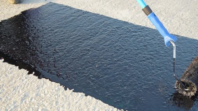Waterproofing coating. Worker applies bitumen mastic on the foundation. Roofer cover the rooftop polymer modified bitumen waterproofing primer, with a roller brush.