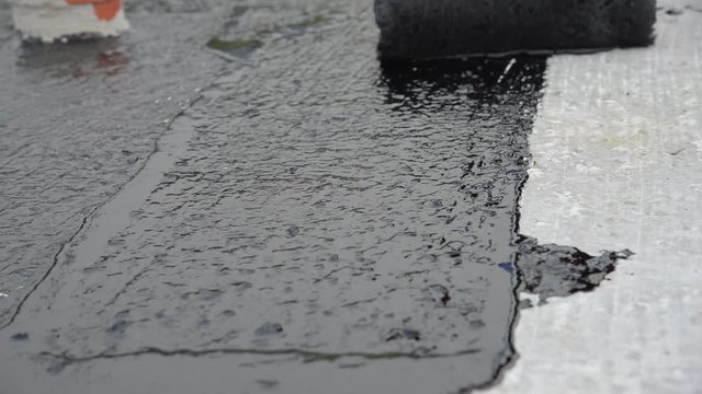 Waterproofing coating. Worker applies bitumen mastic on the foundation. Roofer cover the rooftop polymer modified bitumen waterproofing primer, with a roller brush.