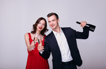 A young lady in a red dress and her boyfriend in a suit are drinking champagne.