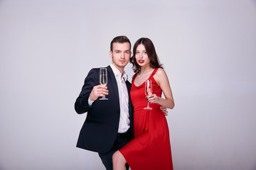 A lady in a red dress with a guy in a suit is drinking champagne.