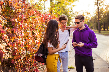 Three teenage friends watching media on a smartphone outdoors.