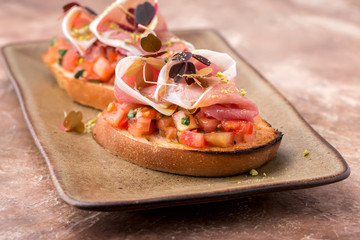 crispy bruschetta, with slices of tomato, Parma ham, on a brown plate, restaurant serving,