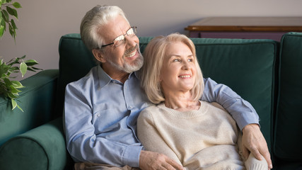 Couple of elderly retirees embracing resting on looking away