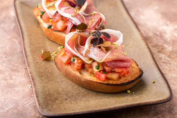 crispy bruschetta, with slices of tomato, Parma ham, on a brown plate, restaurant serving, top view