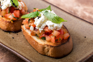 crispy bruschetta, with tomato slices, a bunch of ricotta, Basil leaves, on a brown plate, close-up,Italian concept
