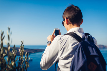 Santorini traveler taking photo of Caldera from Fira or Thera, Greece on phone. Tourism, traveling, vacation concept
