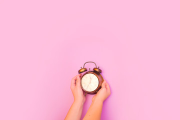 Creative flat lay top view concept of a female hand holding a vintage alarm clock on pink colored paper background with copy space in minimal style, template for text