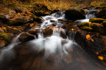 Waterfall on the small river, colorful autumn forest with yellow and orange leaves