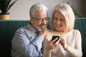 Mature attractive couple sitting on couch using smartphone