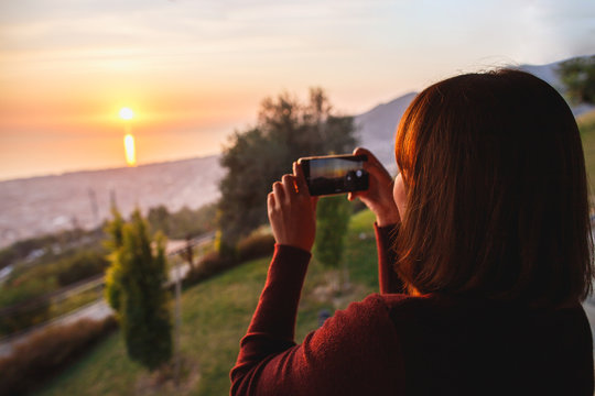 Traveler woman use mobile phone take a photo of beautiful of sunset nature at top of mountain sea view. Deep red sun rays.