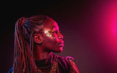 Young African woman with afro hairstyle and golden shiny makeup. Studio shot. Blue and pink neon...