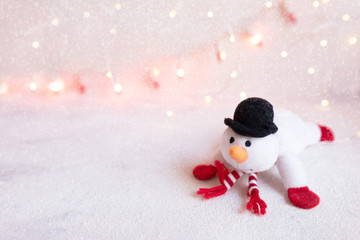 Funny snowman in stylish hat and scarf on abstract christmas lights background. 
