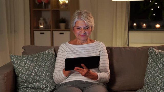 technology, old age and people concept - happy senior woman with tablet pc computer at home in evening