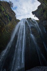 Gljufrafoss (Gljufrabui) waterfall in gorge of mountains. Tourist attraction Iceland near falls of Seljalandsfoss. Man hiker in blue jacket standing on stone and looks at flow of falling water