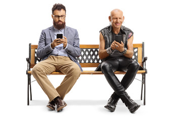 Bearded man and a punker sitting on a bench and typing on mobile phones