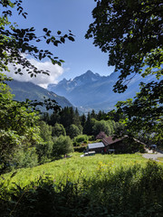 Fototapeta premium A beautiful view of Alpine mountains seen through trees and a cottage down the hill