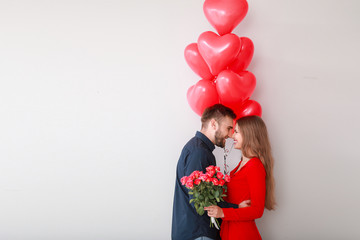 Happy young couple with heart-shaped balloons and flowers on light background. Valentine's Day...
