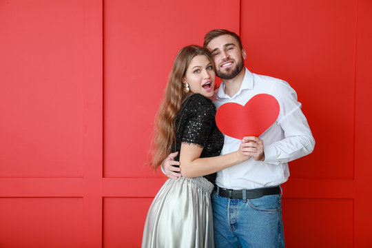 Happy Young Couple With Red Heart On Color Background. Valentine's Day Celebration