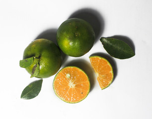 Group of fresh green citrus fruits and their leaves which have orange color inside and slice in different size and set in white color