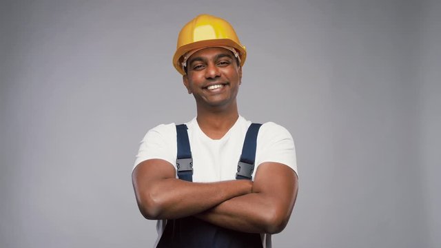 profession, construction and building - happy smiling indian worker or builder in helmet with crossed arms over grey background