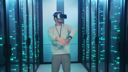 Positive IT engineer wearing virtual reality glasses entertaining having fun during work dancing of joy inside server room. Data center. Humor concept. - Powered by Adobe